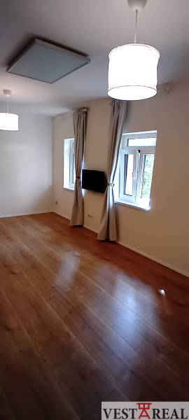 Obývacia izba v rodinnom dome s drevenou podlahou, televízorom a závesmi.