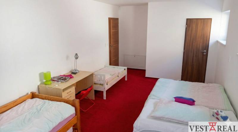 Detská izba v rodinnom dome s tromi posteľami, stolom a červeným kobercom.jpg