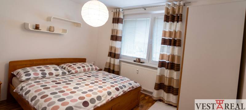 Spálňa s pohodlnou posteľou, vzorovanými závesmi a podlahou s dreveným dekorom v 3-izbovom byte.