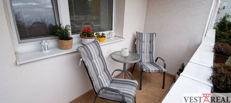 Balkón s dvoma kreslami, stolíkom a kvetmi v 3-izbovom byte.
