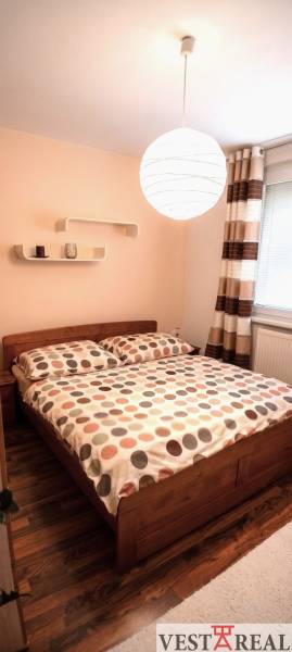 Spálňa s posteľou a podlahou s dreveným dekorom v 3-izbovom byte.