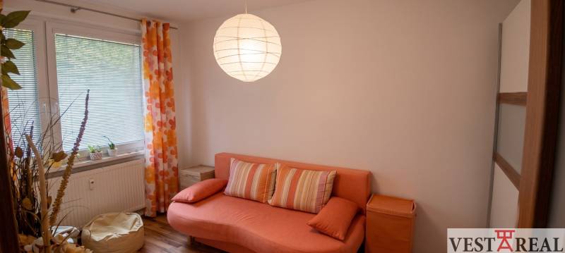 Obývacia izba s oranžovou sedačkou, guľovou lampou a podlahou s dreveným dekorom.