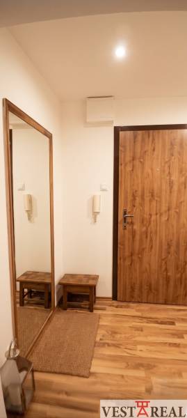 Predsieň s podlahou s dreveným dekorom, zrkadlom a lavicou v 3-izbovom byte.